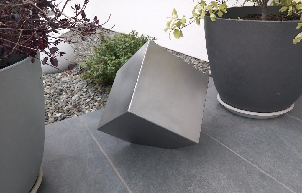 Cube en acier inoxydable, tenu au sol sur un des angles pointus qui donne l'impression que le cube tient en équilibre. Sculpture pour un jardin de 30 centimètres environ.